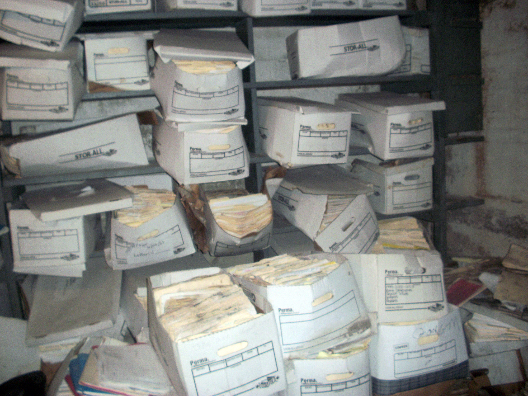 Sagging cardboard boxes of wet moldy paper documents in a basement storage room